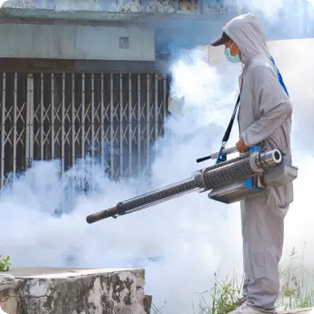 A fumigation expert in Dubai wearing safety gear using a fogging machine outdoors for effective pest and mosquito control.